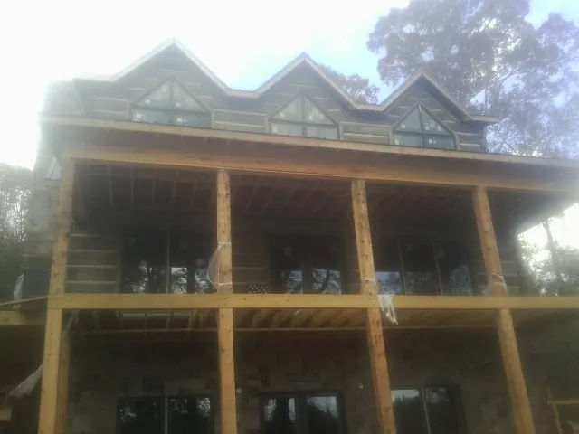 Dormers and porch framing on a large log home under construction — Roof Coating work by our crew in Clayton